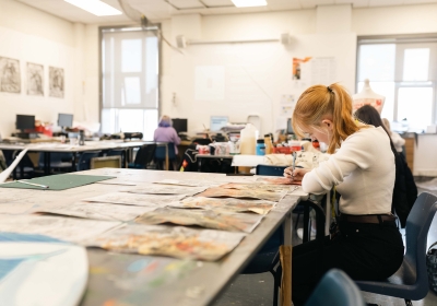 Female Art And Design Student Painting Inside Classroom