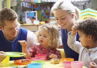 Three Wirral Met Childcare students standing and holding practise babies inside of a classroom