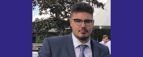 A headshot of new Student Governor Mike Taylor, wearing glasses and a grey suit and tie