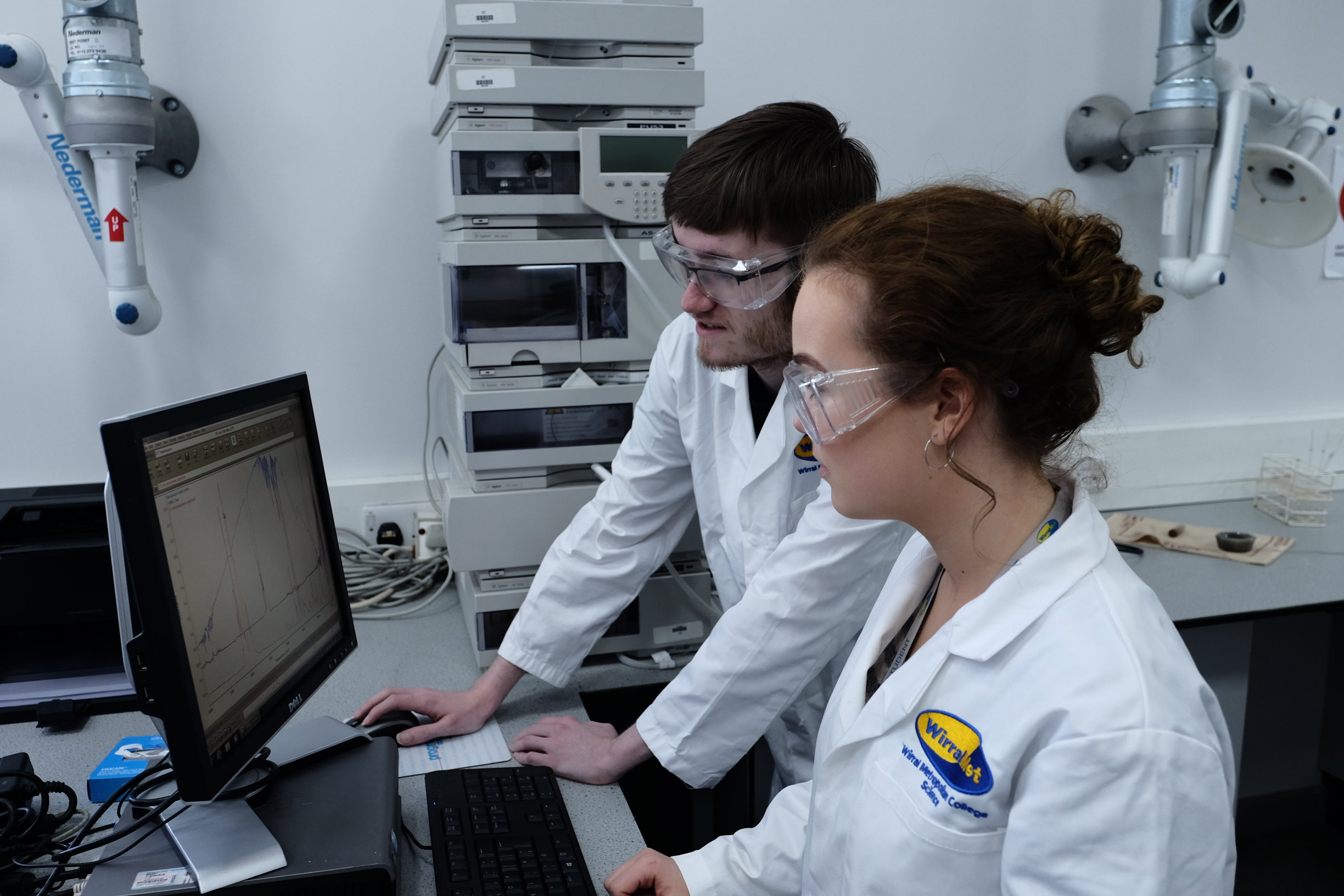 Wirral met College scuience students working on a computer wearing lab coats and safety glasses